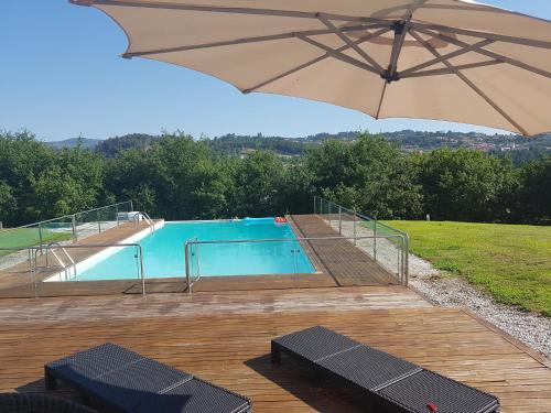 a swimming pool with a large umbrella and benches at Casa de Coyra in Paredes de Coura
