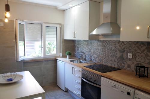 cocina con armarios blancos, fregadero y fogones en Lisbon Beach Apartments 3, en Costa da Caparica