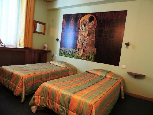 ディーニュ・レ・バンにあるHotel De Provenceのベッド2台が備わる客室で、壁には絵画が飾られています。