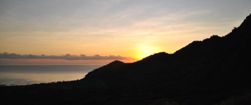 a sunset over a mountain with the sun setting over the water at Tiara Homestay Pemuteran Bali in Pemuteran