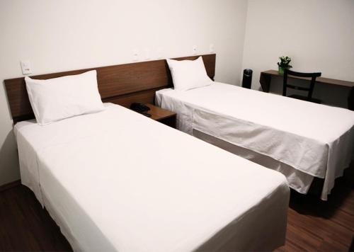 two beds in a hotel room with white sheets at Hotel Galeria in Jales