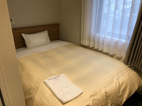 a small bed with a white blanket and a window at Hotel Crown Hills Iwaki in Iwaki