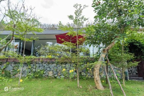 a house with a stone wall and a red umbrella at FLAMINGOS Villa Happy 3 phòng ngủ- view Hồ- bể bơi riêng in Ngọc Quang