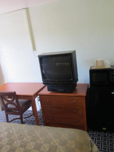 a tv on a wooden dresser with a desk and a table with a bed at Civic Center Lodge / Lake Merritt BART in Oakland