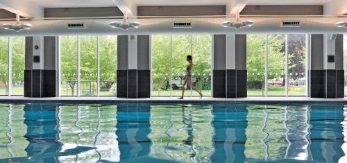 une femme debout en face d'une piscine dans l'établissement The Lensbury Resort, à Richmond upon Thames