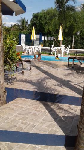 a swimming pool with white chairs and tables and a swimming pool at Pousada Recanto Solar dos Pássaros in Olímpia