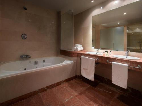 een badkamer met 2 wastafels, een bad en een spiegel bij Parador de Málaga Golf in Málaga