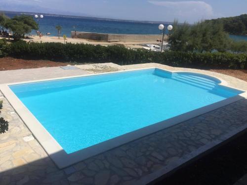 a blue swimming pool with the ocean in the background at Apartmani Villa Dragica in Ugljan