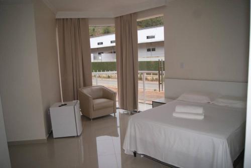 a bedroom with a bed and a chair and a window at Hotel Nardy in Alvinópolis