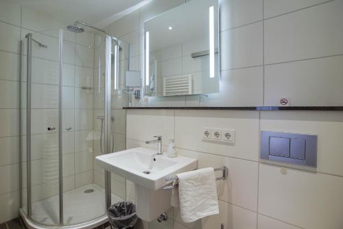 a white bathroom with a sink and a shower at Hotel Maxim in Langenfeld