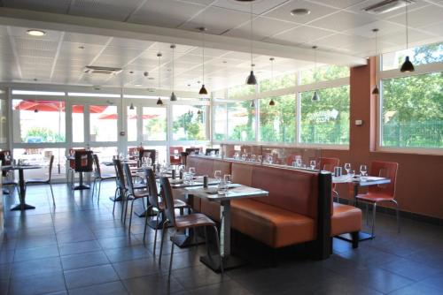 a dining room with tables and chairs and windows at ibis Loriol Le Pouzin in Le Pouzin