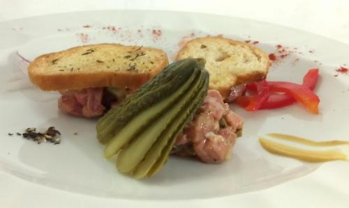 a white plate with a sandwich with pickles and bread at Hotel Mediterraneo in Lignano Sabbiadoro
