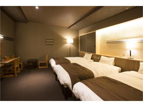 a room with three beds and a table and a desk at Wakkanai Grand Hotel in Wakkanai