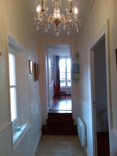 a hallway with a chandelier and stairs with a red chair at L'AURE BLEUE in Bayeux