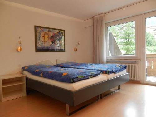 a bedroom with a bed with blue sheets and a window at Artist Apartments & Hotel Garni in Zermatt