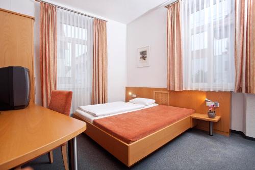 a bedroom with a bed and a desk and a tv at Hotel Gruenshof in Walldorf