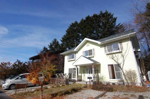 a white house with a car parked in front of it at Guest House Chaconne Karuizawa in Karuizawa