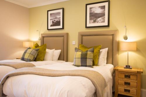 two beds in a bedroom with two lamps and a night stand at Auchrannie Resort in Brodick