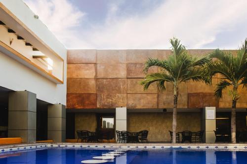 a pool in front of a building with palm trees at Hotel Plaza Mirador in Mérida