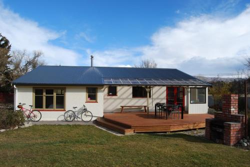 una pequeña casa blanca con terraza y 2 bicicletas en Judge Rock Exclusive Vineyard Cottage Accommodation, en Alexandra