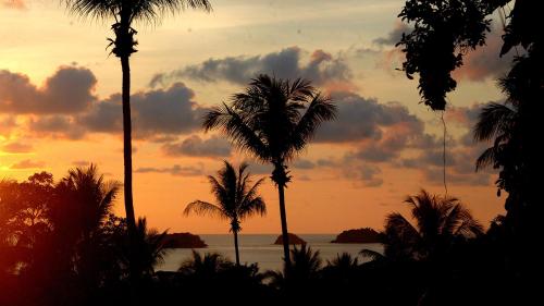 a sunset with palm trees in front of the ocean at Oasis Koh Chang in Ko Chang