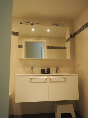 ein Badezimmer mit einem Waschbecken, einem Spiegel und einem Stuhl in der Unterkunft Appartement "FD" in Koksijde