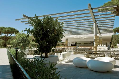 a patio with white chairs and a tree in front of a building at Camping Village Roma Capitol in Ostia Antica