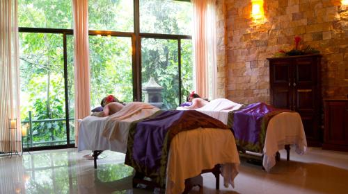 two people laying in beds in a room with windows at Hotel San Bada Resort & Spa in Manuel Antonio