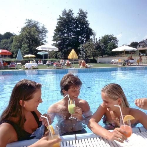 - un groupe de personnes assises dans une piscine avec des boissons dans l'établissement Hotel Velden Bacherlwirt, à Velden am Wörther See