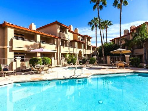 a swimming pool with chairs and umbrellas in front of a building at Gated Mountain View Resort Community, Centrally Located, Three Heated Pool-Spa Complexes, Half-Mile To Hiking! in Phoenix