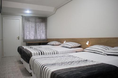 a room with two beds with striped sheets and a window at Hotel Dois Irmãos in Curitiba
