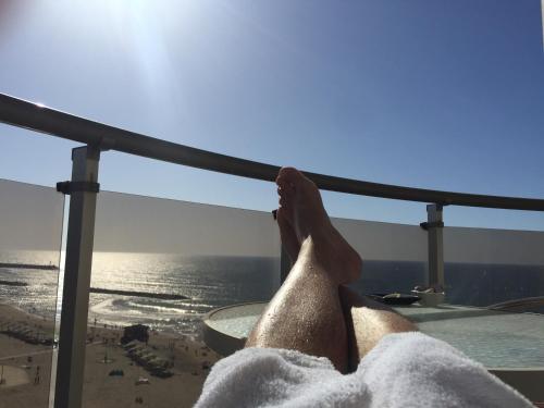 a person with their feet up on a balcony overlooking the beach at Raphael Apartments in Herzelia 
