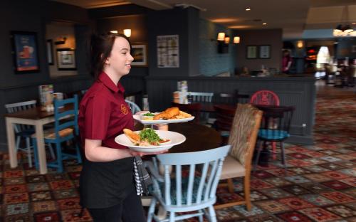 a woman holding two plates of food in a restaurant at Spread Eagle, Gailey by Marston's Inns in Gailey