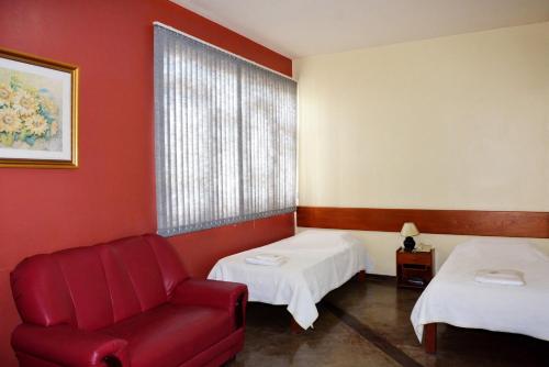Habitación con 2 camas y silla roja. en Ana Maria Apart Hotel en Arcos