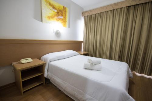 a hotel room with a bed and a side table at Hotel Nacional Inn Poços de Caldas - Lazer completo e Gastronomia no Centro in Poços de Caldas