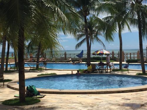 a pool with palm trees and people sitting around it at Residence Kariri Beach Cumbuco in Cumbuco