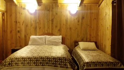 two beds in a room with wooden walls at Cabañas Tunquelen Malalcahuello in Malalcahuello