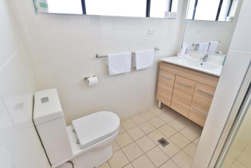 a white bathroom with a toilet and a sink at Coffs Windmill Motel in Coffs Harbour