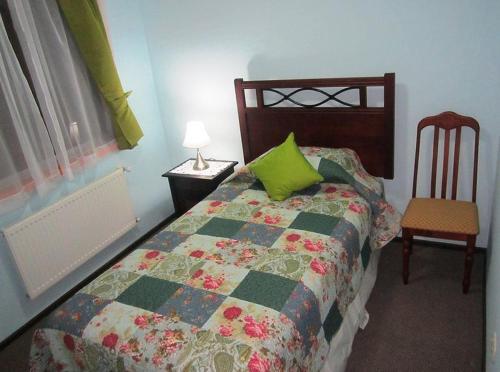 a bedroom with a bed with a green pillow and a chair at Hostal Andalue Temuco in Temuco