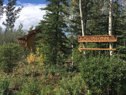 a sign in the middle of a forest at Sawing Logzz Cabin in Copper Center