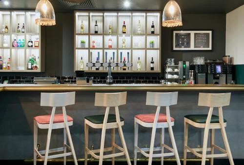a bar with four stools in front of a counter at Leonardo Hotel Manchester Central in Manchester