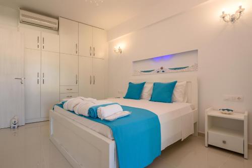 a white bedroom with a large bed with blue pillows at Aristodimos Luxury Apartments in Kalamaki