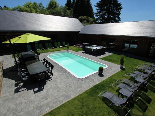 einem Pool mit Stühlen und einem Sonnenschirm neben einem Gebäude in der Unterkunft Beautiful villa with heated outdoor pool in Manhay