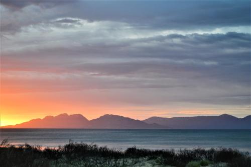 a sunset over the ocean with mountains in the background at Peace & Plenty in Swansea