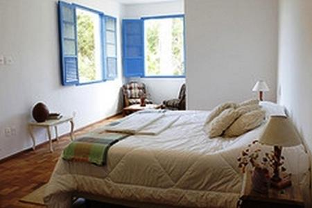 a bedroom with a large bed and two windows at Hotel Fazenda Caco de Cuia in Itabirito