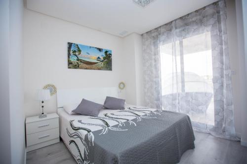 a white bedroom with a bed and a window at Altos del Mediterraneo La Zenia in Los Dolses
