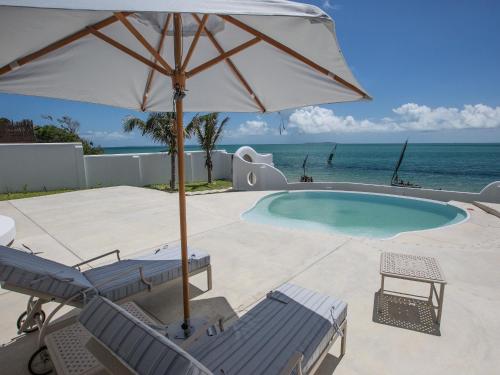 a swimming pool with chairs and an umbrella at Bahia Mar Beach House in Vilanculos