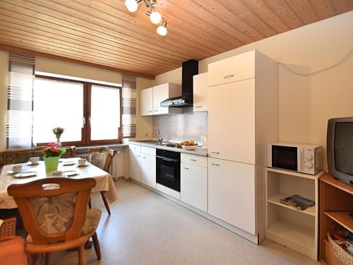 una cucina con armadi bianchi, tavolo e televisore di Charming holiday flat in the Bavarian Forest a Gleißenberg