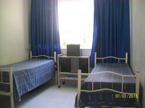 duas camas num quarto com cortinas azuis e uma janela em Apartamento Edificio Mirage em Salvador