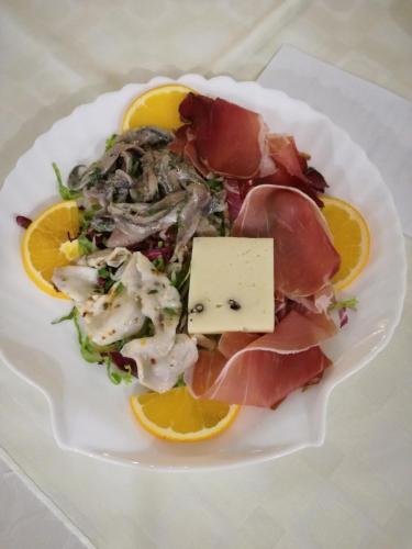 a plate of food with meat and cheese and oranges at Hotel Nike in Giardini Naxos